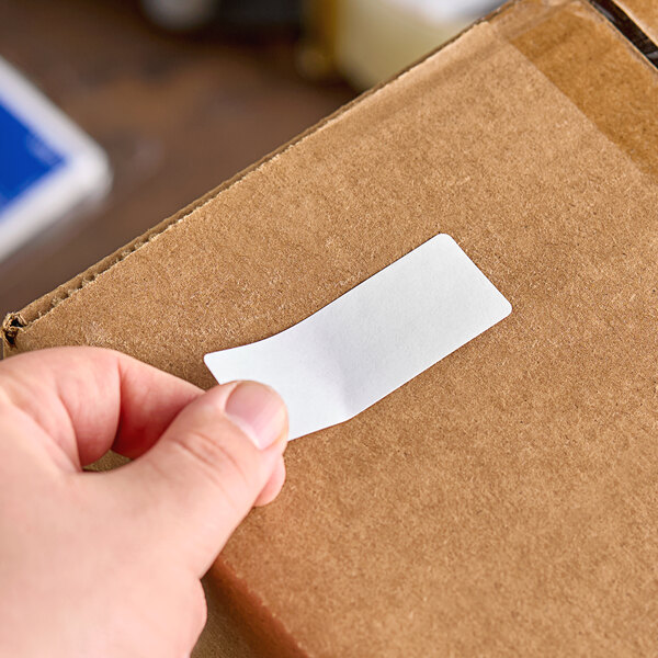 A hand holding a white Avery rectangle label on a cardboard box.