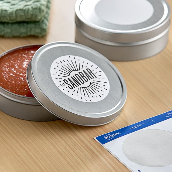 A round metal container with a white label on a table with a jar of red sauce and a paper towel.