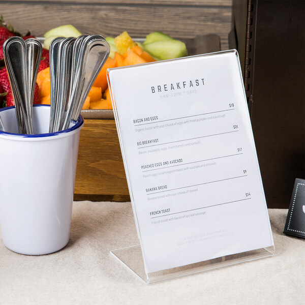 A Cal-Mil easel displayette holding a breakfast menu on a table with a bowl of fruit and a white cup with a blue lid.