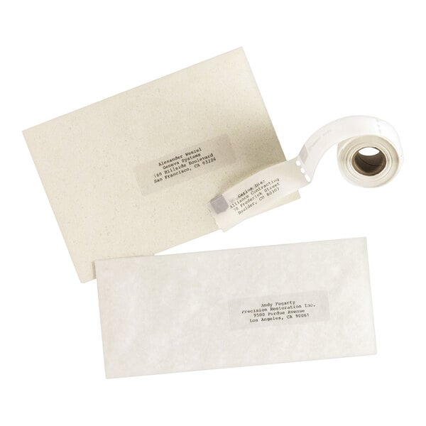 A roll of clear adhesive labels is shown alongside two envelopes, each with a label affixed displaying typed addresses.