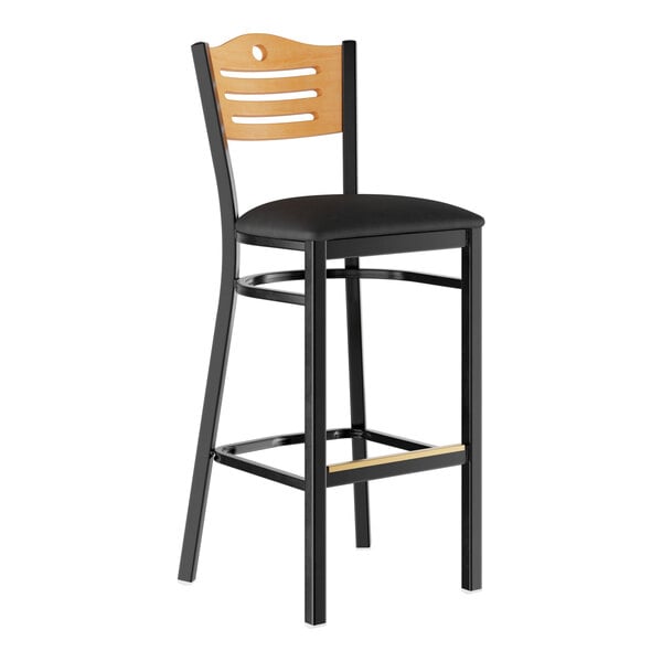 A bar stool with a black padded seat, black metal frame, and a light wood backrest featuring horizontal cutouts.