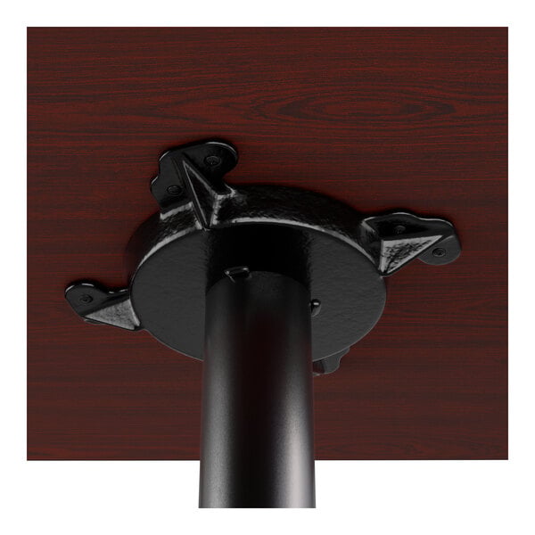 A close-up view of the underside of a dining table showing a black metal base attached to a dark wood tabletop.