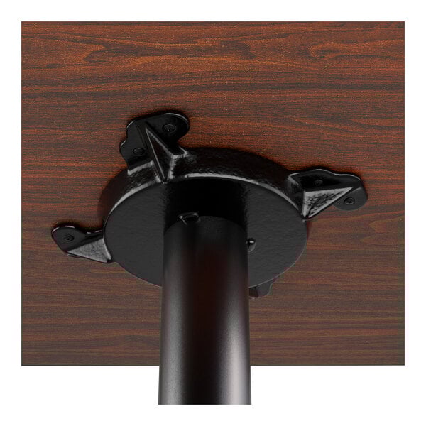 A close-up view of the underside of a wooden table top attached to a black metal pedestal base.