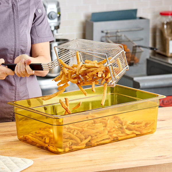 A woman holding a Cambro amber plastic food pan filled with french fries.