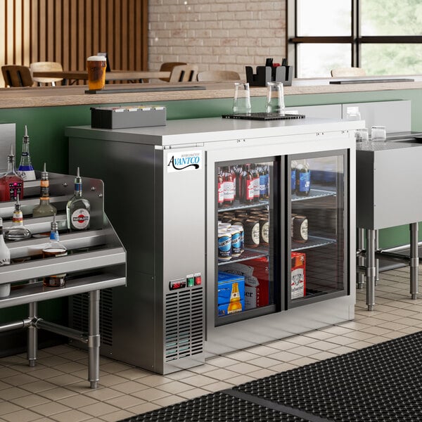 An Avantco stainless steel back bar refrigerator on a metal shelf filled with bottles.
