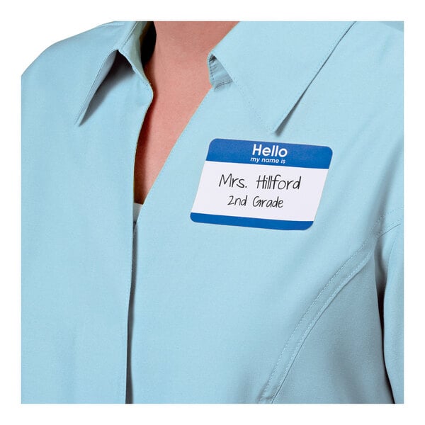 A person wearing a light blue collared shirt with a blue and white name badge sticker that reads "Hello my name is Mrs. Hillford 2nd Grade."