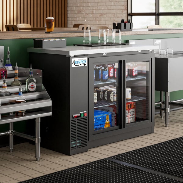 An Avantco black counter height back bar refrigerator with bottles on shelves.