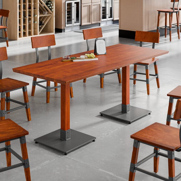 A rectangular solid wood live edge table top with a rustic mahogany finish, set on metal bases in a dining area.