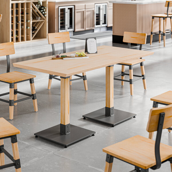 A rectangular solid wood live edge table top with a bleached oak finish, supported by two sturdy metal bases, surrounded by matching wooden chairs in a modern dining setting.