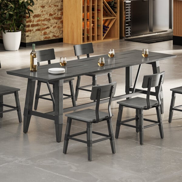 A rectangular dining table with a slate gray finish, surrounded by matching chairs, set with glasses, a wine bottle, and plates in a modern kitchen setting.