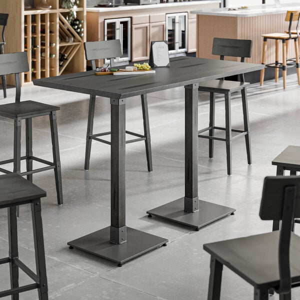 A Lancaster Table & Seating industrial live edge bar height table with a slate gray finish and chairs in a room.