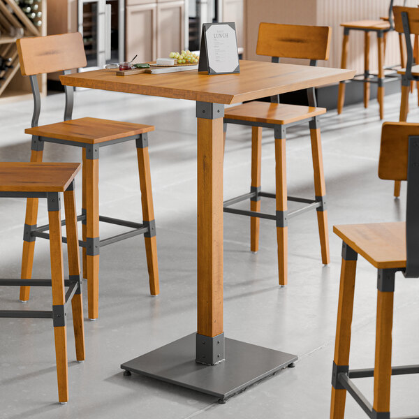 A Lancaster Table & Seating solid wood live edge bar height table with a honey maple finish and four stools in a room.