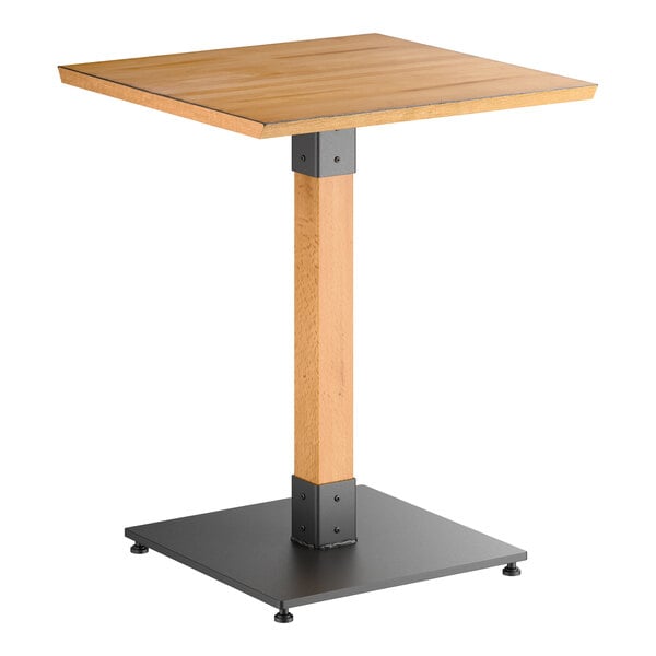 A square wooden table with a honey maple finish, supported by a single central wooden leg and a black metal base.