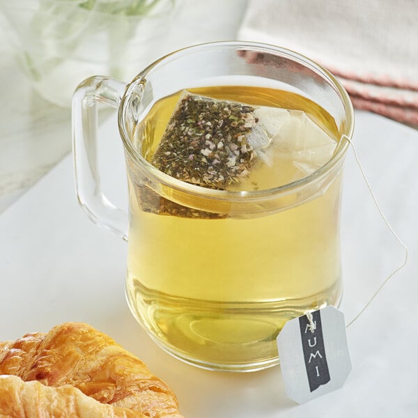 A glass mug of Numi Organic White Rose Tea with a tea bag in it on a white saucer.