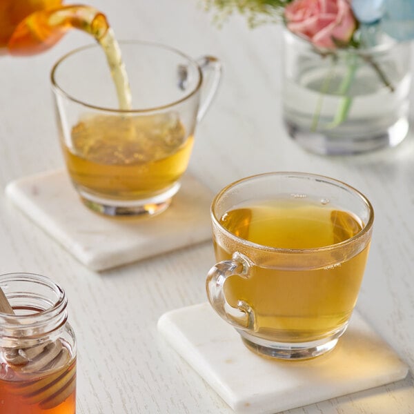 A glass cup of Numi Organic Jasmine Green tea on a table with a jar of honey and a spoon.