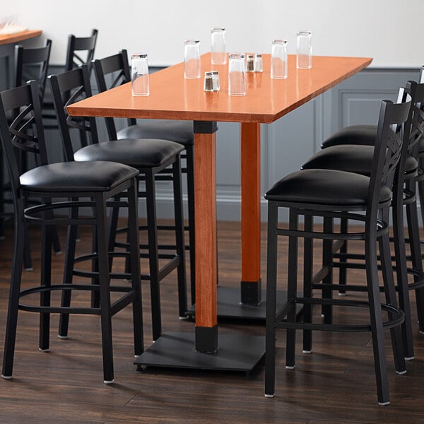 A Lancaster Table & Seating live edge bar height table with glasses on it and black chairs around it.