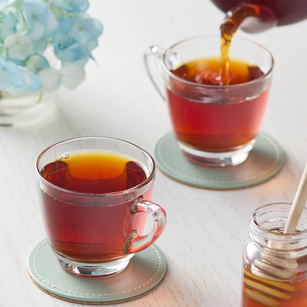 A glass cup of Numi Organic Breakfast Blend Loose Leaf Tea with a jar of honey and a wooden spoon on the table.