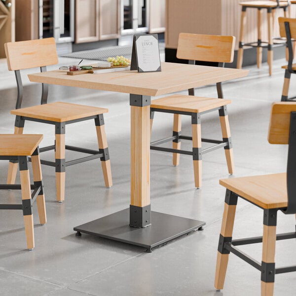A square industrial-style table with a bleached oak finish and a sturdy metal base, surrounded by matching chairs.