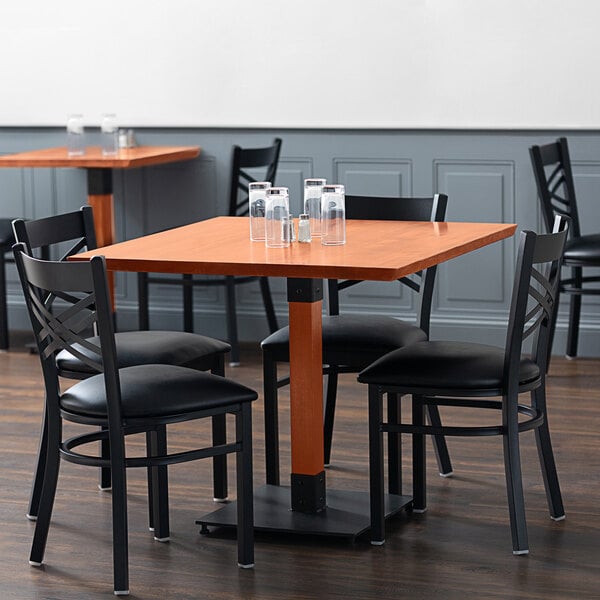 A Lancaster Table & Seating standard height table with a rustic mahogany finish and live edge top with black chairs in a restaurant.