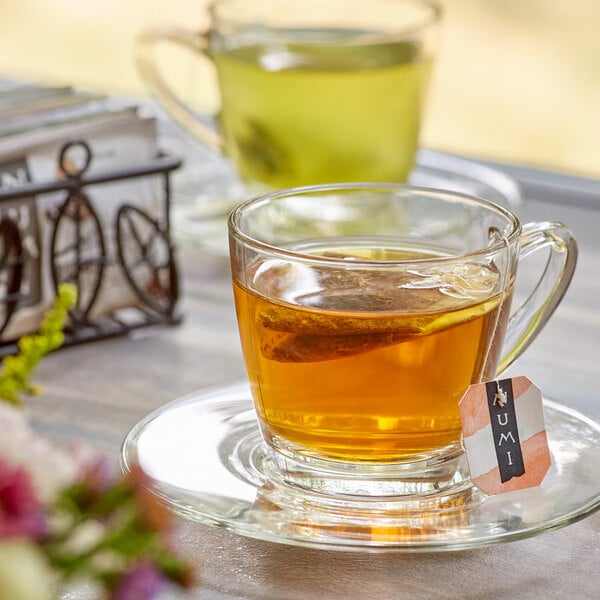 A glass cup of Numi Organic tea on a saucer with a tea bag label.