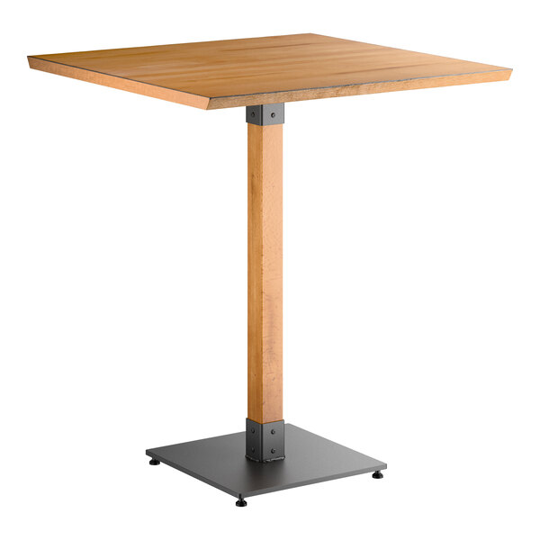 A square wooden bar-height table with a honey maple finish, supported by a single central wooden leg and a square metal base.