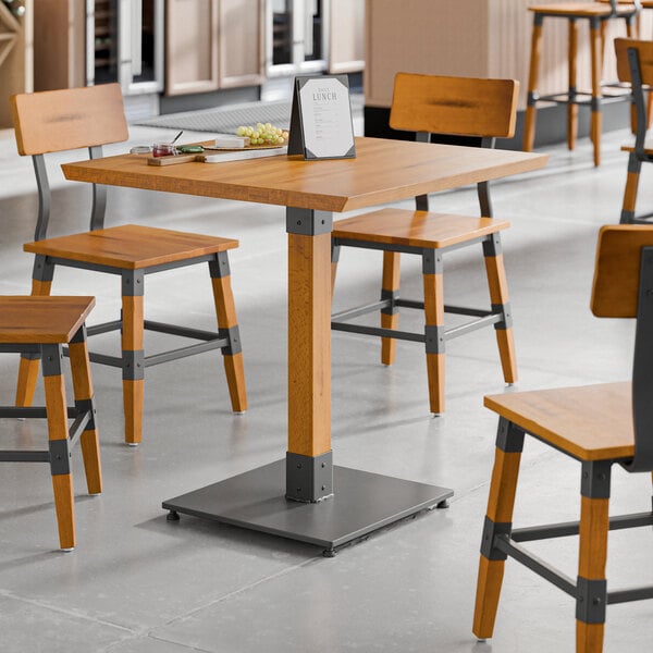 A square industrial-style table with a honey maple finish and a sturdy metal base.