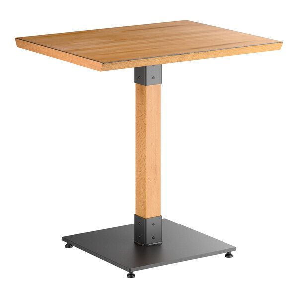 A rectangular wooden table with a honey maple finish, supported by a central wooden pedestal and a black metal base.