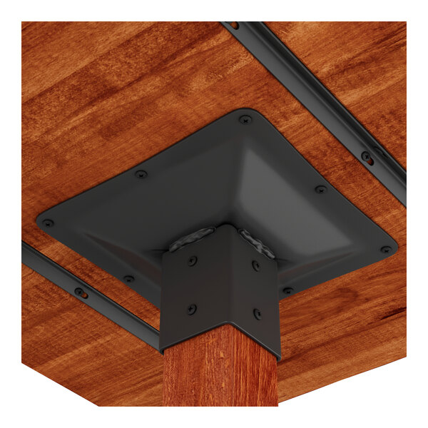 A close-up view of the underside of a wooden table with a rustic mahogany finish, showing a metal bracket securing the leg to the tabletop.