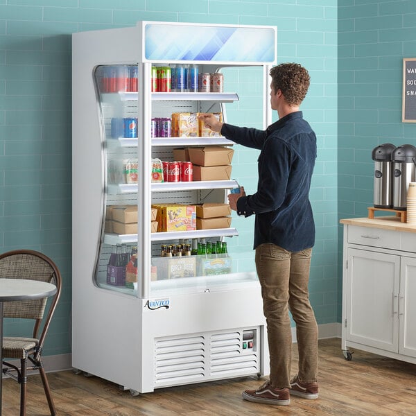 An Avantco white refrigerated air curtain merchandiser with a man opening it.