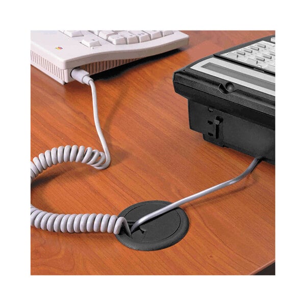 A black Master Caster adjustable grommet with a telephone cord plugged into a hole in a desk.