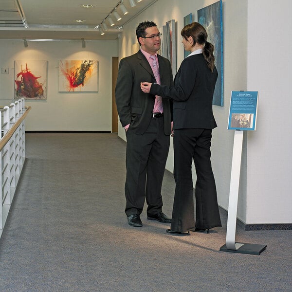A man in a suit talking to another man using a Durable metal stand with an adjustable insert space.