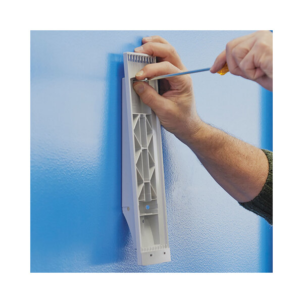 A person installing a white plastic Durable wall shelf using a screwdriver.