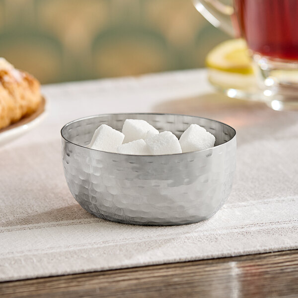 An American Metalcraft stainless steel sauce cup filled with sugar cubes on a table.