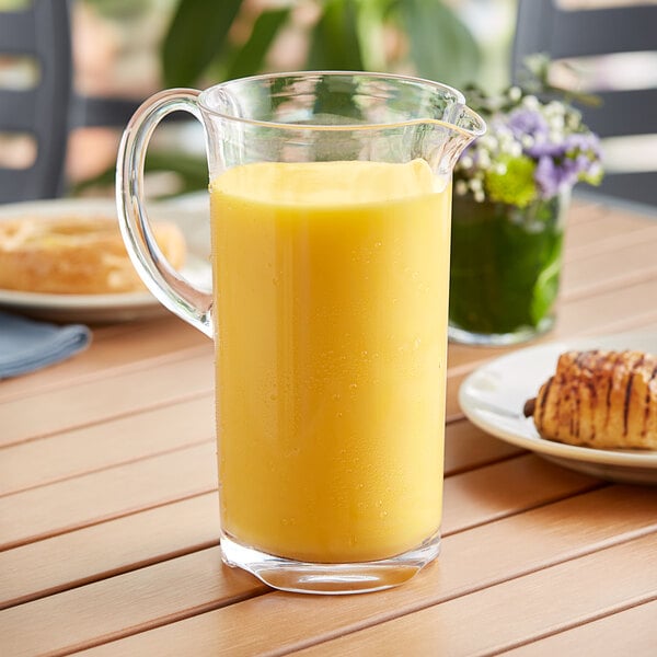 A Libbey plastic pitcher of orange juice on a table next to a plate of food.