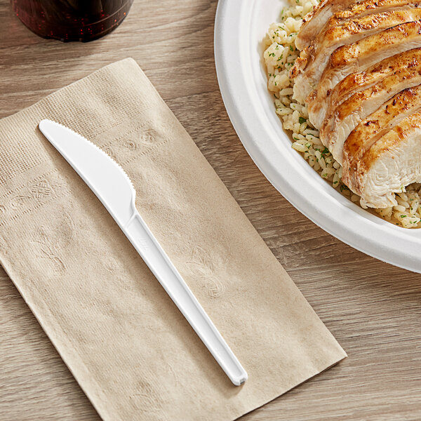 A plate of food with a white EcoChoice compostable plastic knife on a napkin on a table.