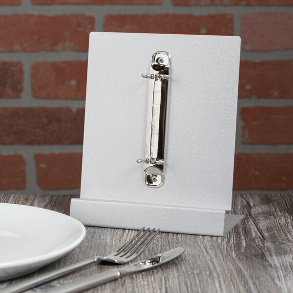 A Menu Solutions aluminum menu tent on a table with a plate and utensil.
