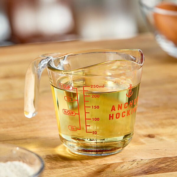 A clear glass Anchor Hocking measuring cup with liquid in it on a kitchen counter.