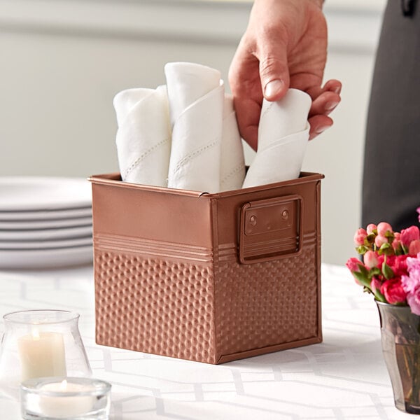 A person putting napkins in a square hammered copper utensil holder.