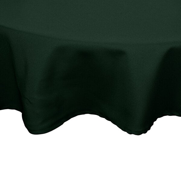 A hunter green poly/cotton blend round table cover with hemmed edges.