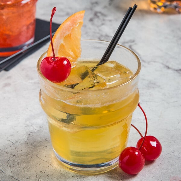 A Libbey Tritan plastic rocks glass with yellow liquid, ice, and orange and cherry garnish.