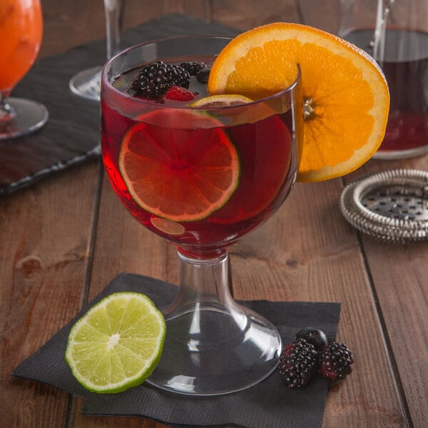 A Libbey plastic schooner filled with red liquid and fruit slices on a table in a cocktail bar.