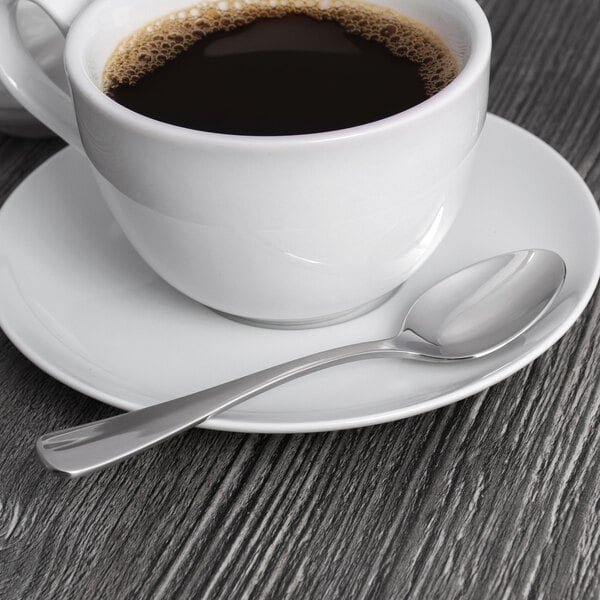 A cup of coffee on a saucer with a Oneida Baguette stainless steel teaspoon.