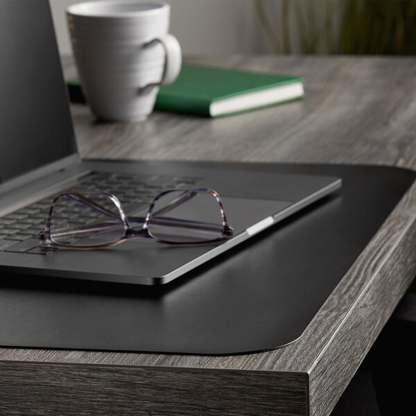 A black ES Robbins vinyl desk pad with a laptop, book, and white mug on it.