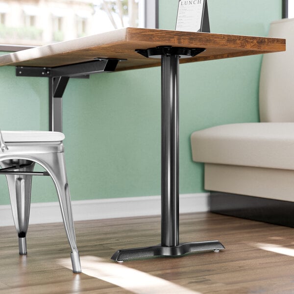 A Lancaster Table & Seating black cast iron end column table base with a white chair at a restaurant table.