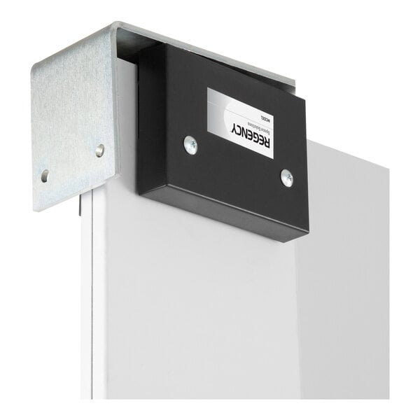 A close-up view of a metal bracket and black box mounted on the top edge of a white panel or door.