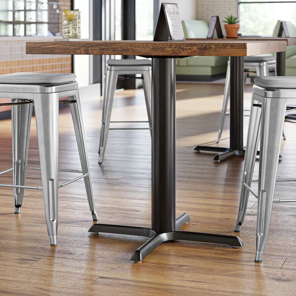 A Lancaster Table & Seating black cast iron counter height table column on a table with stools in a restaurant.