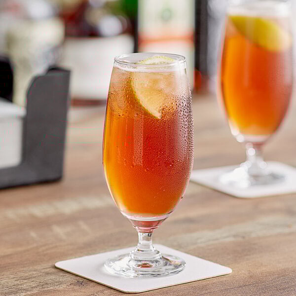 Two Acopa stemmed iced tea glasses on a table with iced tea and lemon slices.