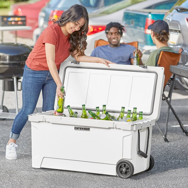 A woman and man wearing hats putting bottles of beer into a white CaterGator outdoor cooler.