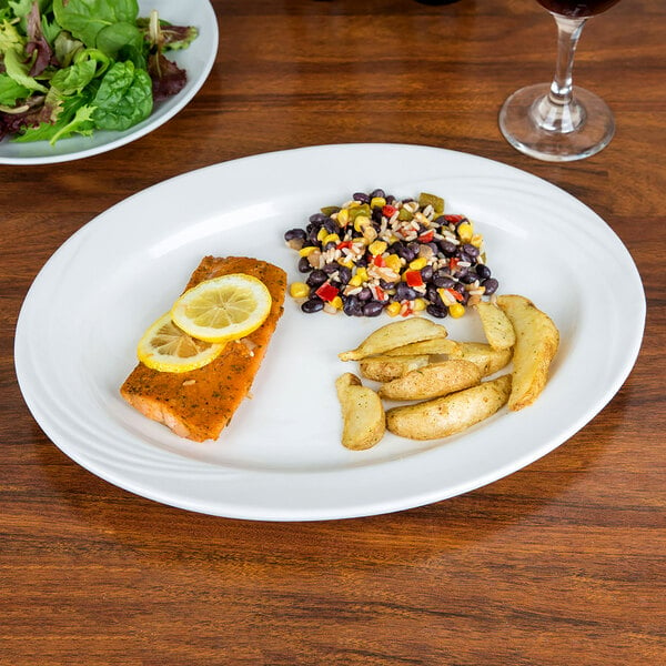 A CAC Garden State oval porcelain platter with a plate of green and red salad and a lemon slice on the side on a table.