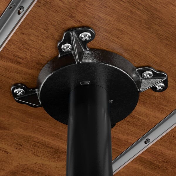 A close-up view of the underside of a rustic walnut solid wood live edge bar height table showing the metal mounting bracket and support pole.